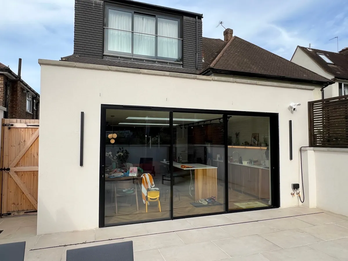 Three-panel Cor Vision (InfiniGLIDE 3) slim sliding doors in black across a rendered rear extension, looking into an open-plan kitchen