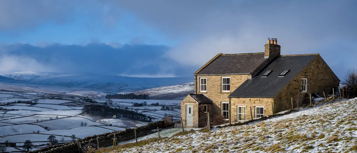 Stone farmhouse with sash windows above snowy hills